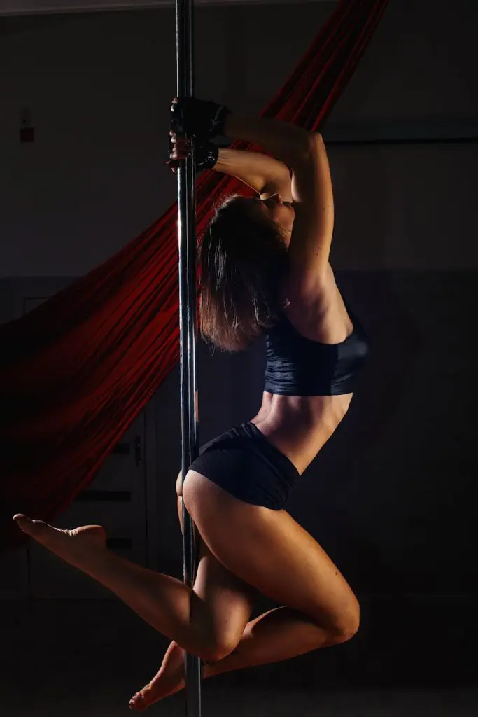 woman in black sports bra and black shorts doing posing on a dance pole, strip club near atlanta airport